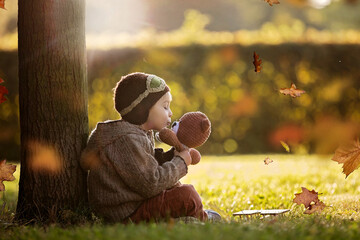 Little toddler child, boy, playing with airplane and knitted teddy bear in autumn park