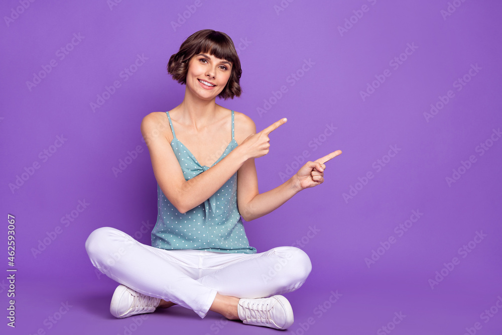 Canvas Prints Portrait of attractive cheerful girl sitting on floor demonstrating copy space isolated over bright violet purple color background