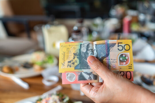 Woman's hand holding Australian notes to make a payment in restaurant.