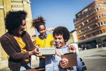 Young mixed race family with present outdoor.Mother and daughter giving a gift box to father.