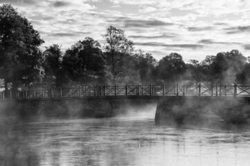 Grayscale photography of bridge, lake and mist. A beautiful morning as the fog swirls around the landscape.  Black and white picture, place for text, copy space.