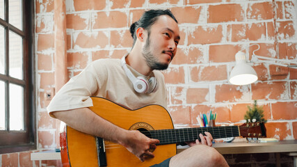 Artists producing music in their home sound studio, Asian man playing guitar and singing in living...