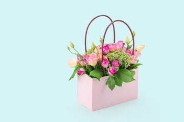 A bouquet of flowers in delicate pink tones with green leaves in a gift bag with handles on a blue background. Side view. Copy space. Postcard. Layout for the design.