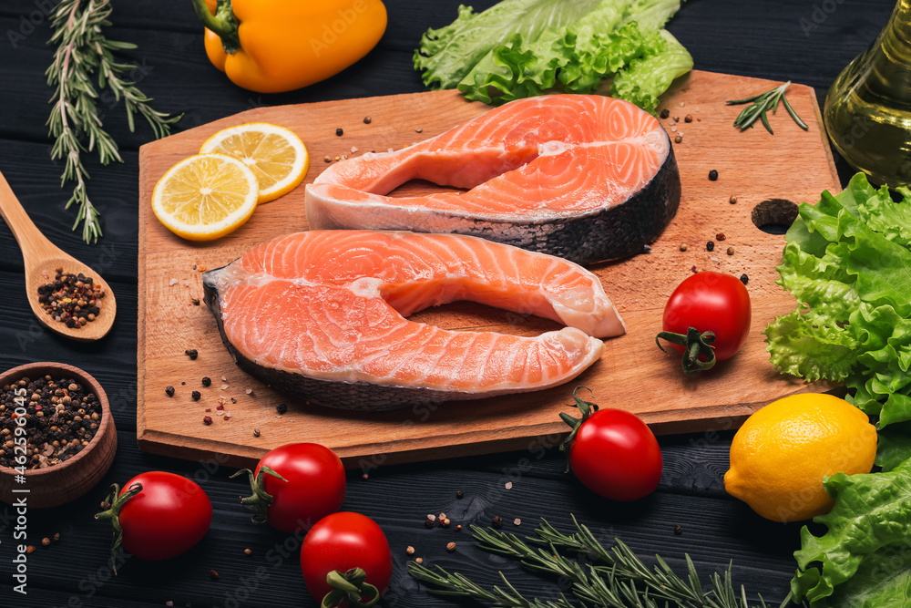 Wall mural two salmon steaks on a wooden board with lemon, tomatoes, rosemary, pepper, spices. dark background.