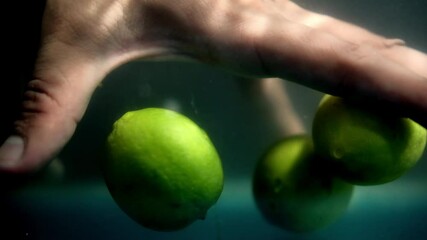 Hands slowly grabbing three fresh limes from underwater - Powered by Adobe