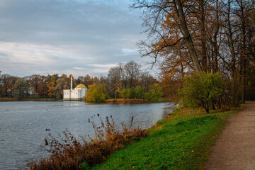 Fototapeta na wymiar View of the alley along the Big Pond in the Catherine Park of Tsarskoye Selo and the Turkish Baths pavilion in the background on an autumn cloudy day. Pushkin, St. Petersburg, Russia