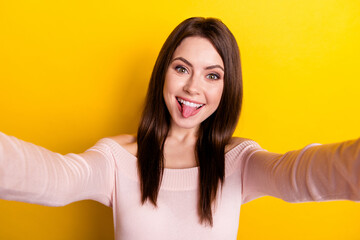 Photo of young funky funny cheerful good mood woman taking selfie showing tongue isolated on yellow...
