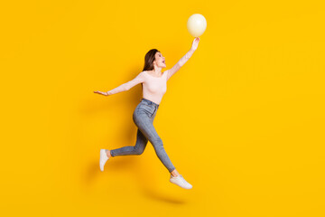 Full size profile side photo of young happy excited cheerful woman running in air with balloon isolated on yellow color background