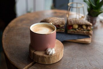 One Cup of cappuccino with latte art. Coffee in pink cup and sandwich with ham, cheese, bacon, tomatoes in cafe. Concept of easy breakfast. Rustic style