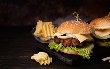 A set of homemade delicious burgers of beef, onion, cheese and lettuce on a dark wooden background