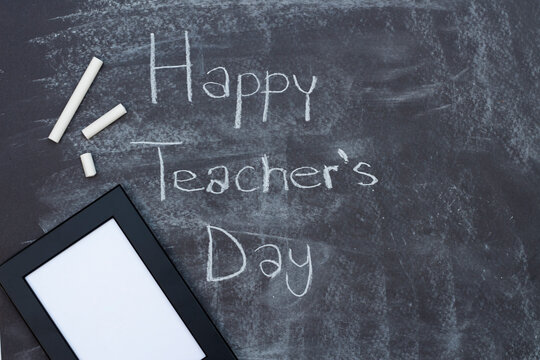 Teacher's day text, a blank photo frame and chalk on blackboard background. Mockup, top view. Happy teachers day