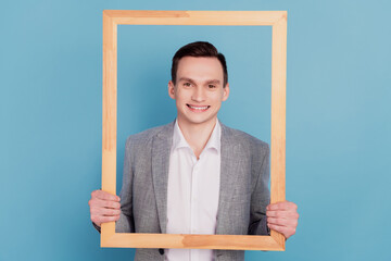 Portrait of funky cheerful handsome man hold wooden frame make picture isolated over blue color...
