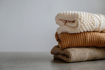 Bunch of knitted warm pastel color sweaters with different knitting patterns folded in stack,...