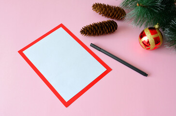 writing christmas letter, decorated with pine branches with cones and christmas sphere on pink background