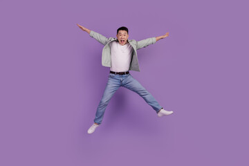 Photo of crazy excited asian man jump have fun isolated violet color background
