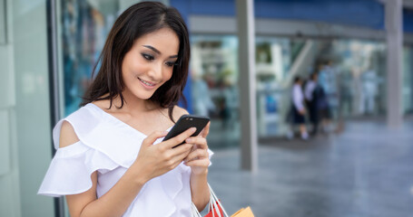 Portrait Asian beautiful happy young woman smiling cheerful and she using smartphone paymetn for shopping online  with shopping bags