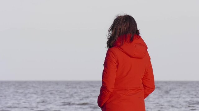A Woman in a Red Jacket Looks at the Foamy Waves. Windy Autumn Day at the Shore of Lake Ilmen. Northern landscape