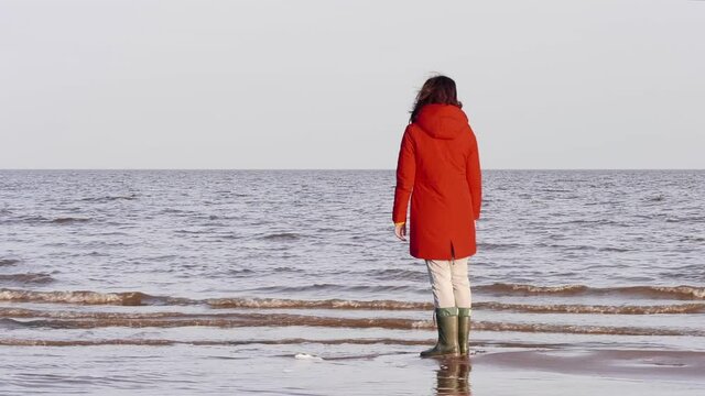 A Woman in a Red Jacket Walks on the Shore of a Lake In Windy and Cold Autumn Weather. Windy Autumn Day at the Shore of Lake Ilmen. Northern landscape