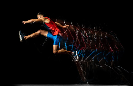 Full-length portrait of young man, professional track athlete, runner in a jump, training isolated over black background. Stroboscope effect.
