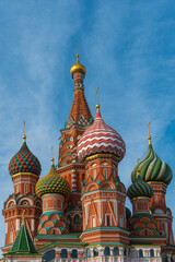 Fototapeta na wymiar View of the multicolored domes and brick walls of St. Basil's Cathedral against the background of blue sky and light clouds, vertical Moscow photo