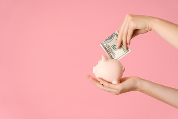 Piggy bank on a woman's palm, the hand puts a hundred-dollar bill on a pink background in the money box