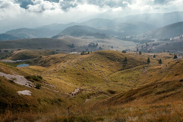 Dramatic landscape with green hills and sheep grazing in the distance. Cascades of beutiful mountains under the clouds somewhere in the north of Italy