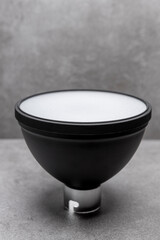 Vertical frame with small speedlite flash light modifier reflector and diffuser cap on top for illumination against a modern contemporary gray background. Photography accessory studio still life.