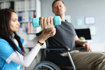 Rehabilitation therapist helping disabled man in wheelchair to lifting dumbbell in closeup