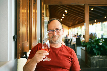 Portrait of middle age man in indoor restaurant, holding glass of wine