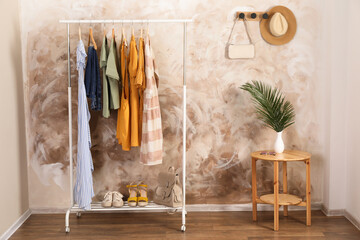 Different stylish clothes hanging on rack in room