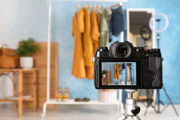 Rack with stylish clothes and mirror near light blue wall indoors, focus on camera screen. Space...
