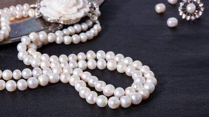 White luxurious pearl necklace on a black leather background. Shiny iridescent  pearl jewelry close up. 