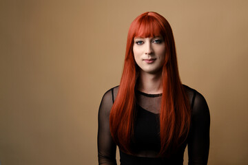 Transsexual woman. Portrait of young transgender woman in a red wig and makeup on a brown background. Concept diversity, transsexual, and freedom. - obrazy, fototapety, plakaty