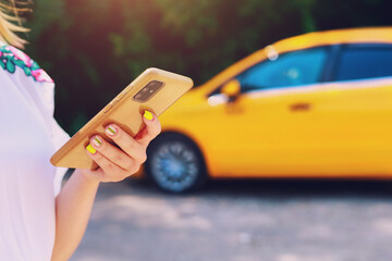 Smartphone or phone in female hands on a blurred background of a yellow taxi service car