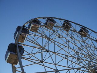 White metal construction of an attraction Ferris wheel with observation cabs high against a blue sky