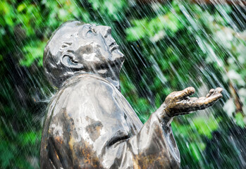 Pomnik w parku na tle drzew. Padający deszcz z fontanny.