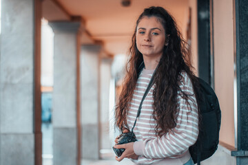 Adolescente turista de cabello oscuro realizando fotografías por la ciudad en su viaje junto con equipaje de mochila para capturar momentos 