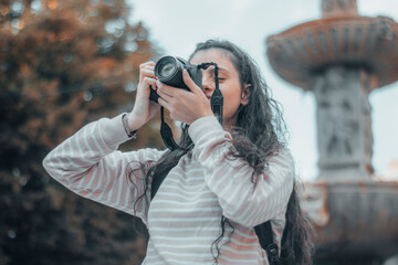 Fotógrafa profesional realizando una sesión fotográfica en un parque de la ciudad de Nueva York para su trabajo mientras está viajando con su equipaje de mochila junto con una sonrisa de alegría