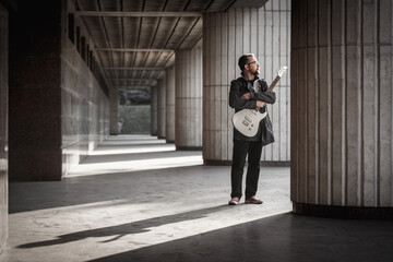 Man in black with a beard with electric guitar on urban outdoor location.