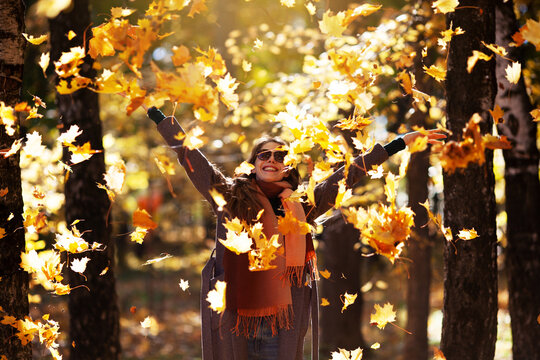 Joyful young woman throws maple leaves on a sunny day in autumn