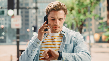 Portrait of a Stylish Man in Casual Clothes is Being Late, Checking His Watch, Making a Call with His Smartphone. Handsome Young Man Walking in Hurry in a Big City Street. He is Focused.