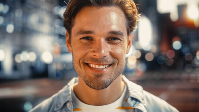 Portrait Of A Happy Handsome Young Man In Casual Clothes Standing On The Street At Sunset. Stylish Male Model In Big City Living The Urban Lifestyle. Background With Office Buildings And Billboards.