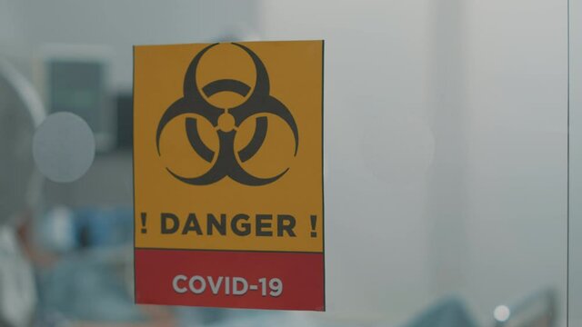 Close up of danger sign against coronavirus outbreak in hospital ward. Infectious zone in isolation and quarantine against covid 19 pandemic with biohazard symbol on glass. Lockdown virus area