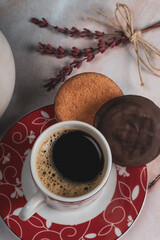 Taza blanca y roja de café negro, con dos galletas de chocolate y un delicado bouquet de lavanda roja atada con cuerda natural, sobre una mesa de piedra de mármol rosa.