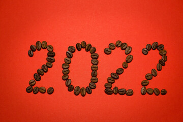 The numbers 2022 on a red background with white snowflakes. Figures 2022 from coffee beans. Coffee beans. New Year 2022. White snowflakes on a red background.