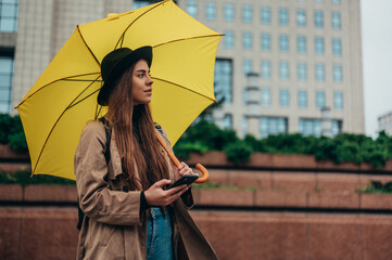 Young beautiful woman using a smartphone and holding a yellow umbrella
