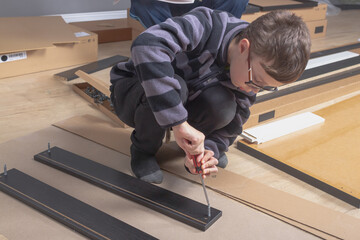 A teenage boy installation, assembly furniture in his room, a teenager screws into wooden furniture