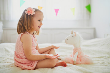 Adorable little girl in pink dress playing with unicorn