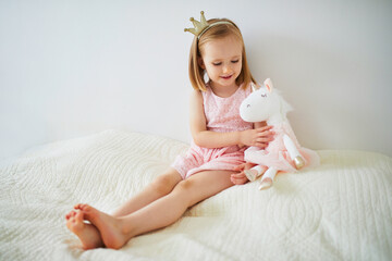 Adorable little girl dressed as princess playing with unicorn