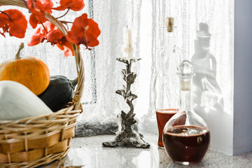 Autumn still life. Basket with pumpkins, candlestick with a candle and decanter with red wine on windowsill during the day time